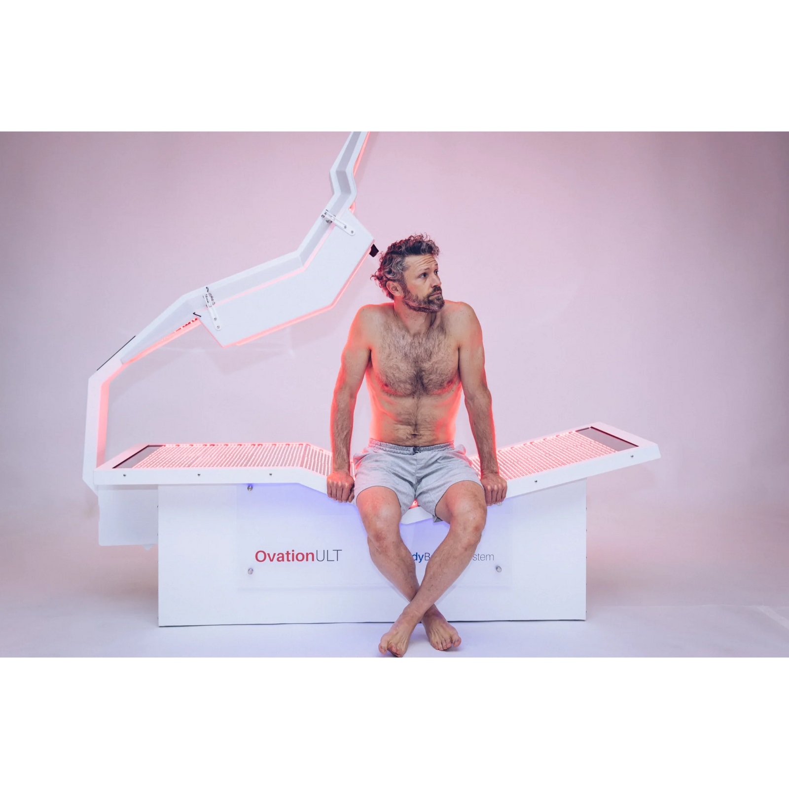 Body Balance System OvationULT Zero Gravity Red & Infrared Light Bed – man sitting on the bed in pink light
