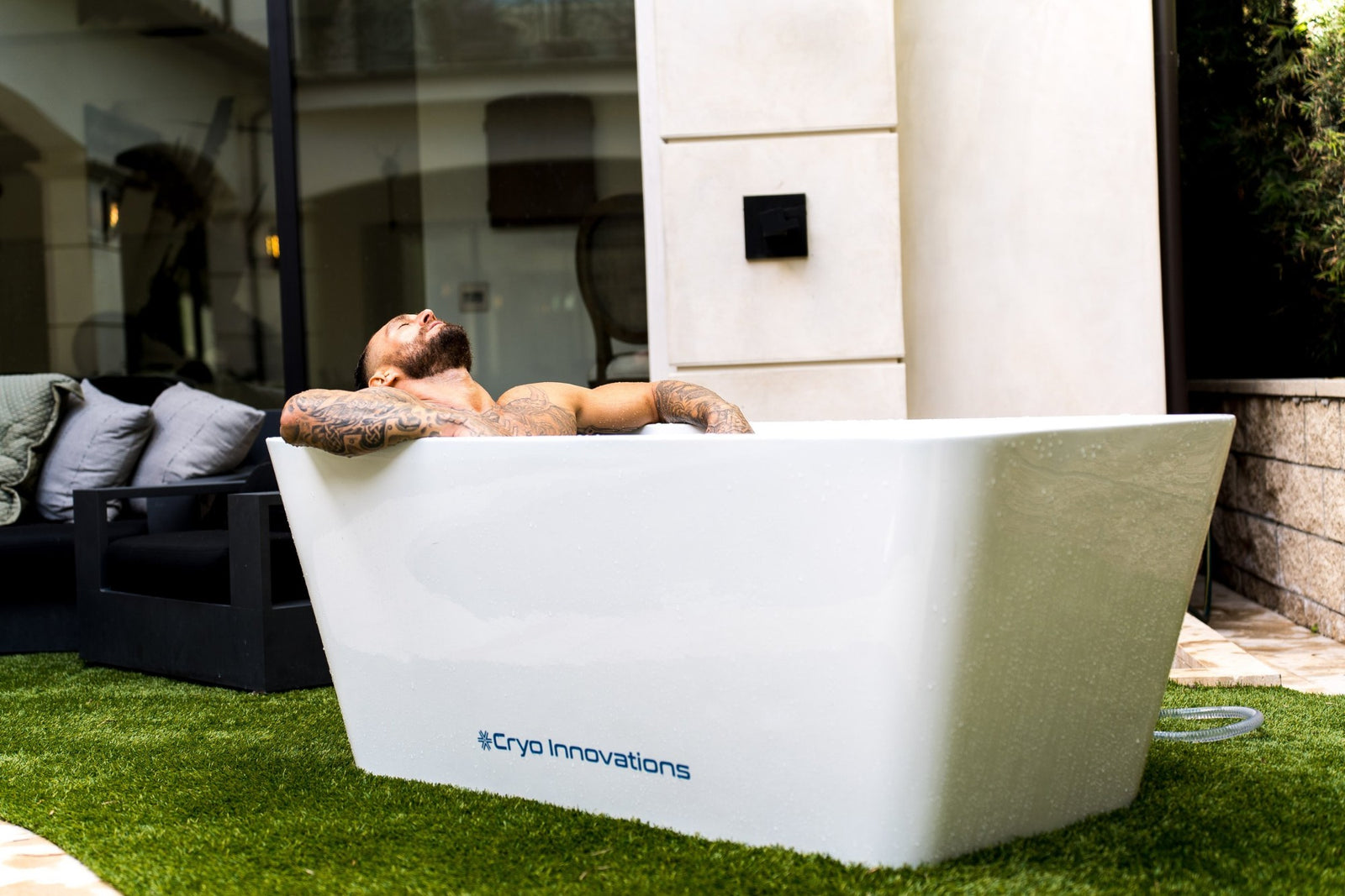 Cryo Innovations XR Cryo Plunge white acrylic tub on a lawn with a person seated in it