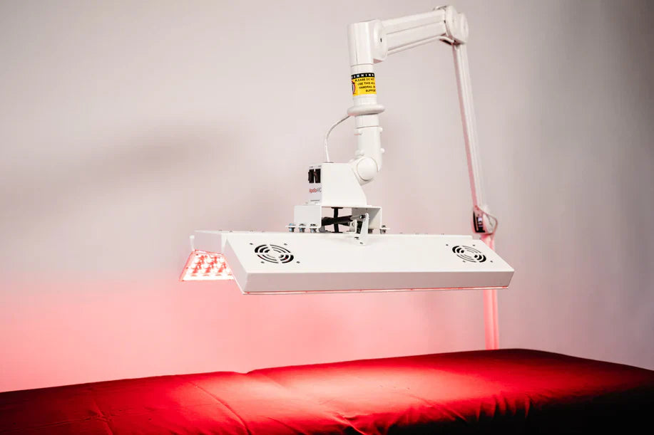 ApolloARC red light therapy panel glowing over red treatment bed with adjustable arm