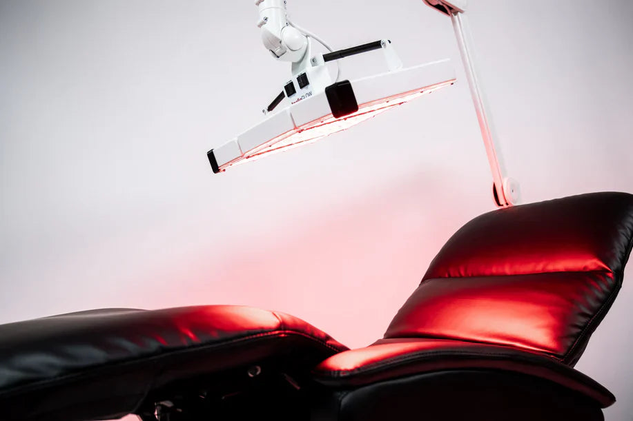 ApolloGLOW red light therapy panel suspended above black leather recliner chair