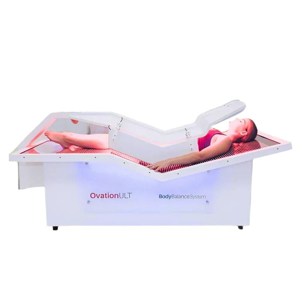 Woman lying inside the OvationULT red light therapy bed during a full-body treatment.