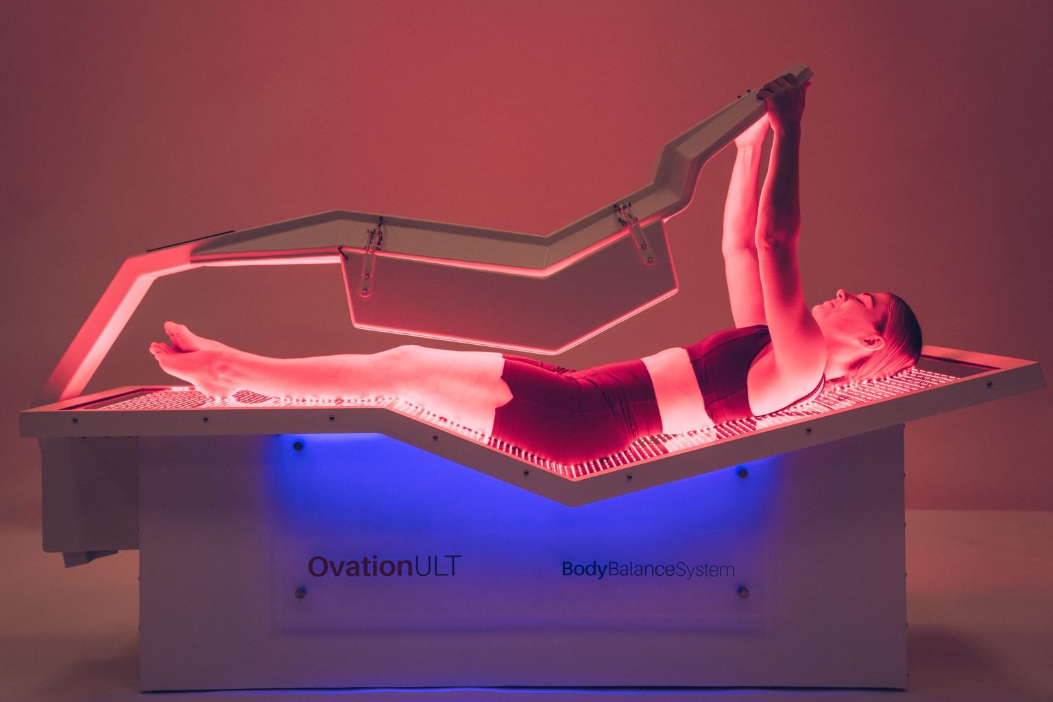 Woman using OvationULT full-body red light therapy bed with canopy in zero-gravity position
