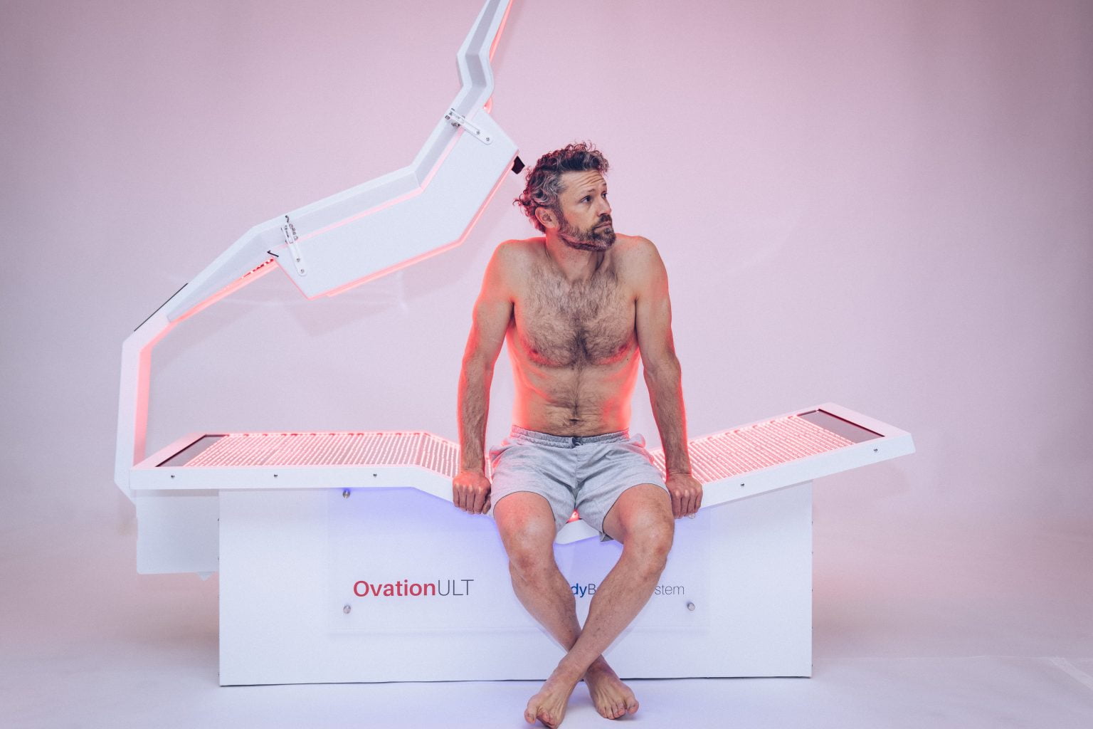 Man sitting on OvationULT red light therapy bed before starting treatment session.